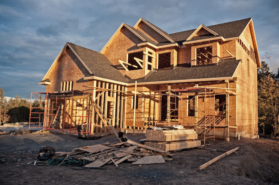 A picture of a construction site with a house in the process of being built and wood in the front yard.